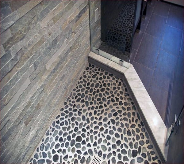 Shower floor with dark pebble stones, glass enclosure, and textured stone walls.