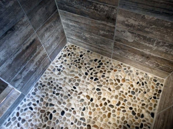 Shower floor with natural pebble stones and rustic wood-look tiled walls.