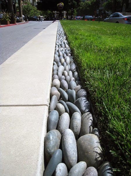 Concrete curb with a pebble-filled drainage border alongside a neatly trimmed lawn.