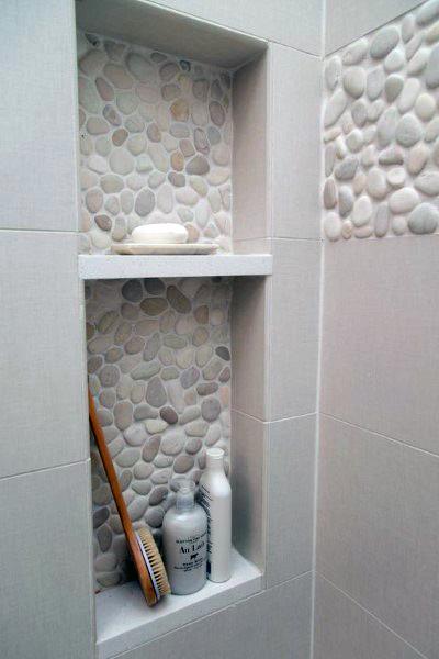 Pebble accent tile shower niche with soft tones and built-in shelves for toiletries.
