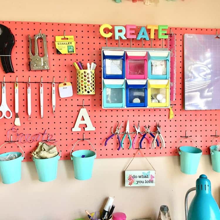 Colorful craft room pegboard with tools, storage bins, and decorative buckets, "CREATE" sign at the top
