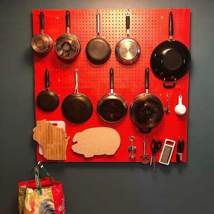 red pegboard in kitchen holding pots and pans