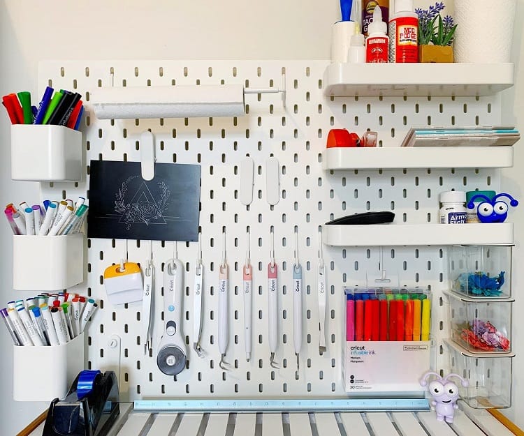 Organized pegboard with art supplies, markers, scissors, and craft materials neatly arranged against a white wall