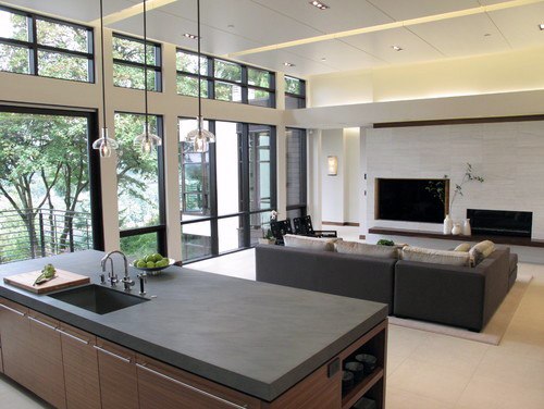 Modern open living room with large windows, an island kitchen, gray sofa, and a wall-mounted TV