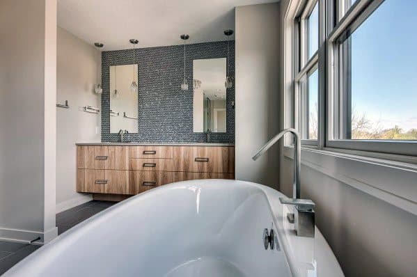 Modern bathroom with freestanding tub, wooden vanity, and glass mosaic tile accent wall.