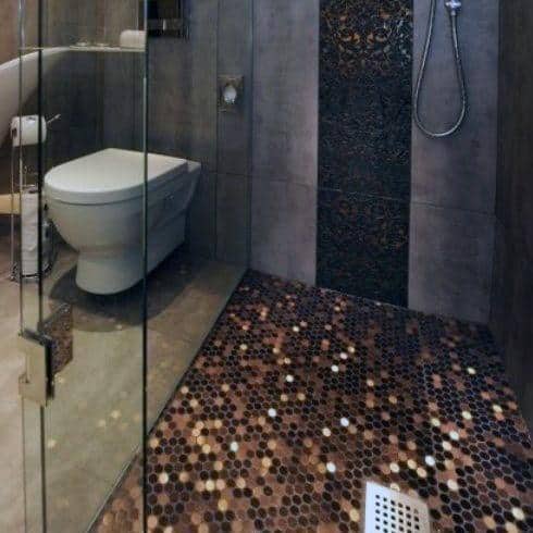 Modern bathroom with penny tile shower floor, glass enclosure, and dark textured walls.