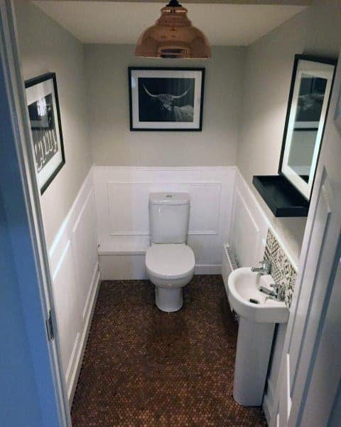Small bathroom with penny tile floor, framed artwork, and white wainscoting walls.