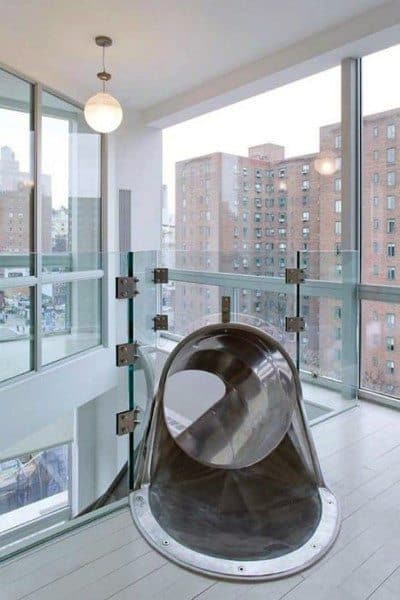 A sleek, modern slide descends from a high-rise apartment, offering city views through expansive windows