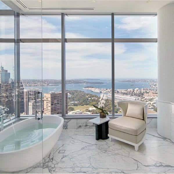 Luxurious white bathroom with cityscape view, featuring a modern tub and plush chair