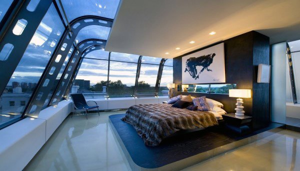 Modern bedroom with curved glass walls, city skyline view, and artistic decor.