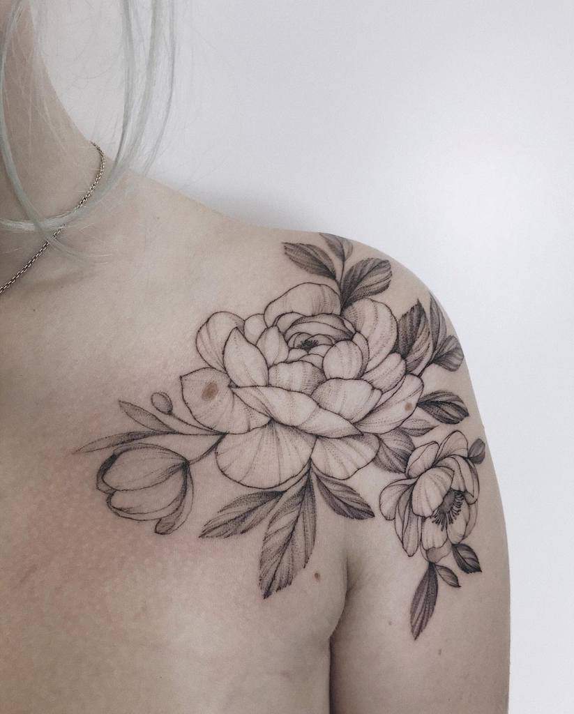 A stunning floral tattoo adorns the shoulder, showcasing detailed peonies and leaves intricately inked in black