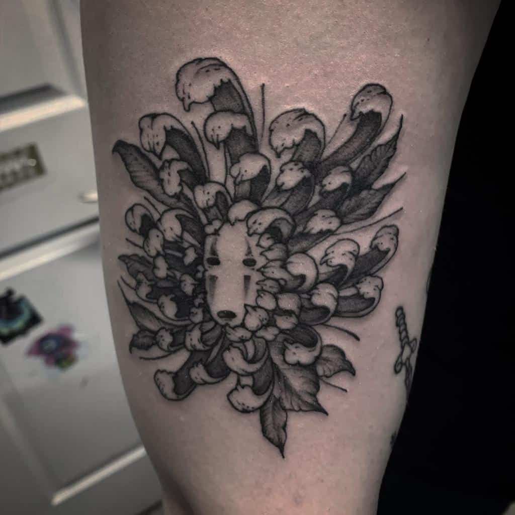 Intricate black ink tattoo of No-Face’s mask from Spirited Away blended into a chrysanthemum with dripping petal effects