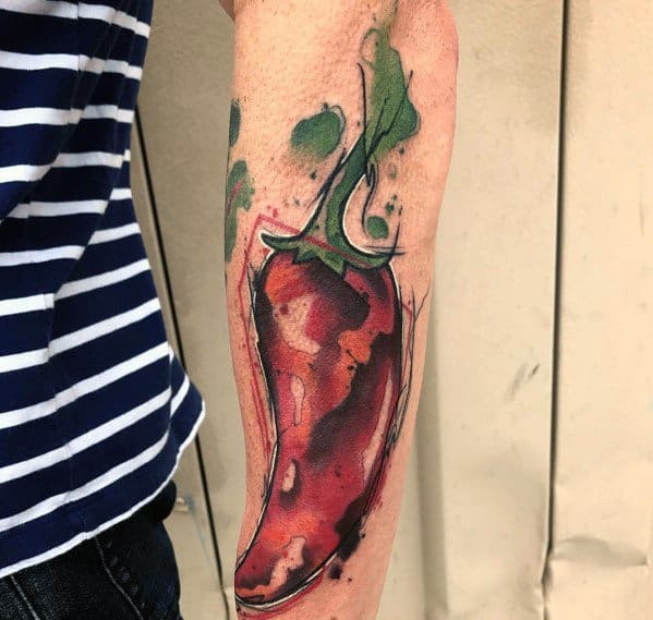 Watercolor-style chili pepper tattoo on the forearm with bold red tones, splashes of green, and abstract shading for a vibrant and artistic look.