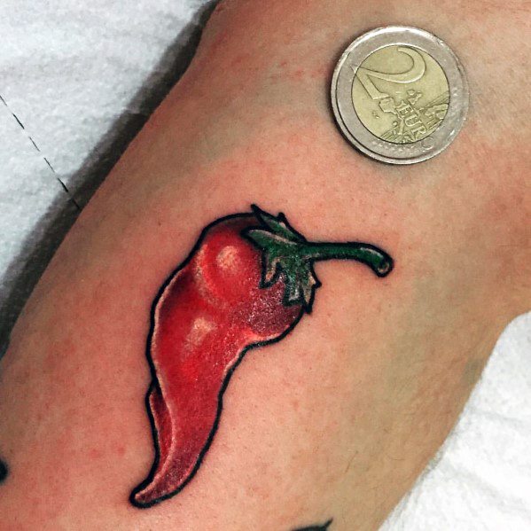 Small red chili pepper tattoo with bold shading and a green stem, placed near a two-euro coin for scale, creating a vibrant and realistic design.