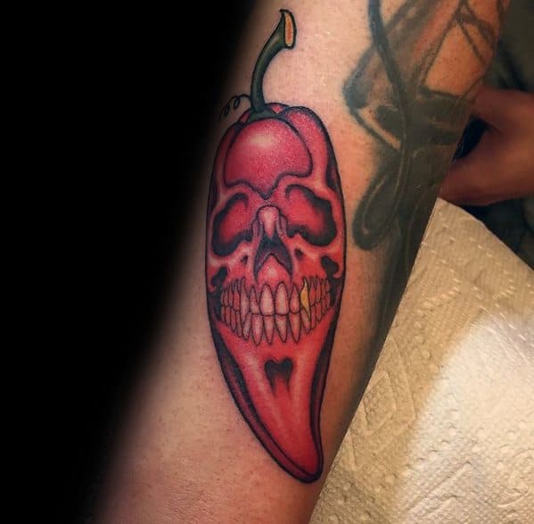 Red chili pepper tattoo with a detailed skull design integrated into its surface, featuring bold shading for a striking and eerie look.