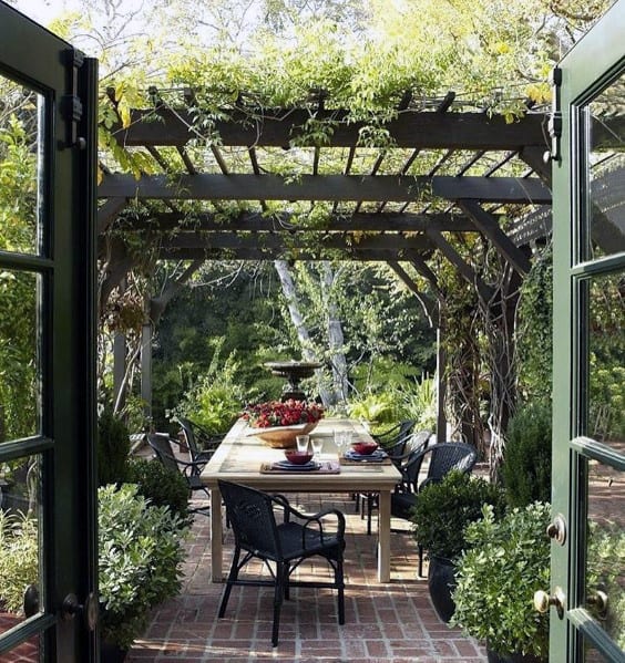 Outdoor pergola with a dining table, surrounded by brick pathways and lush trees