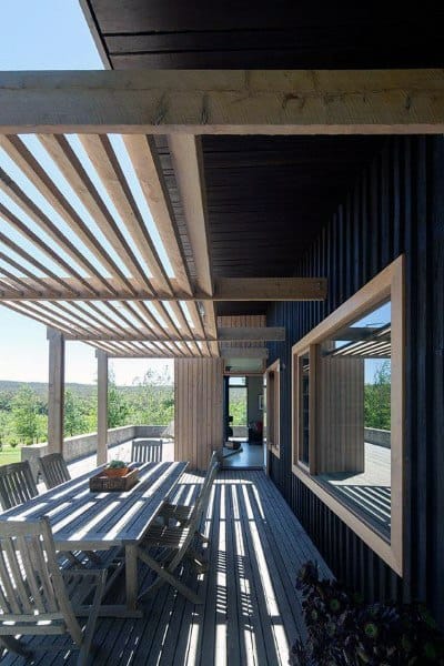 Modern pergola with wooden slats, outdoor dining table, and a sleek black-paneled wall.