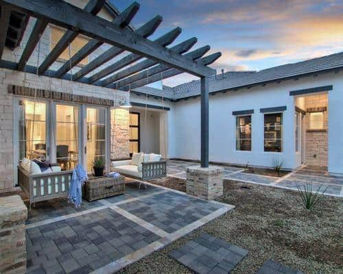 Modern pergola with dark wood beams, hanging chairs, brick accents, and a stylish paved patio.