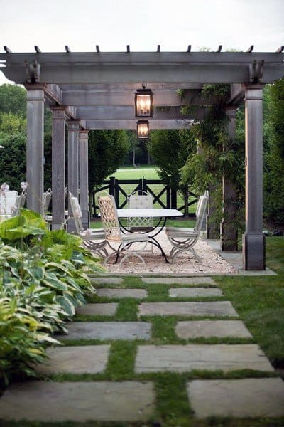 Elegant pergola with lantern lighting, dining setup, and a garden path leading to a gate.