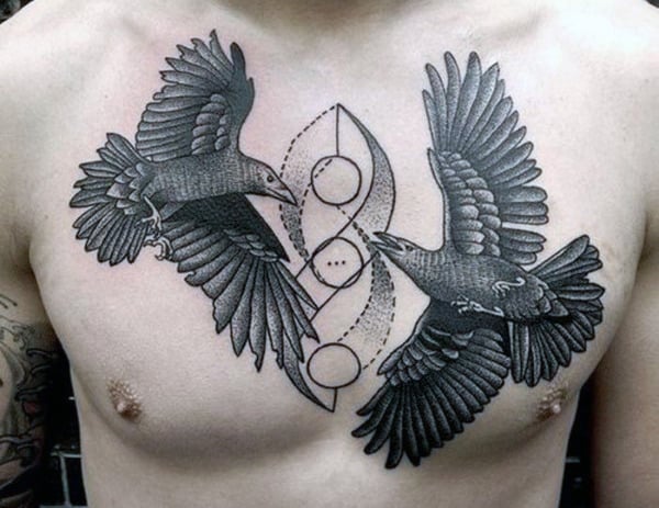 Two detailed black crow tattoos facing each other on a person's chest with a geometric design
