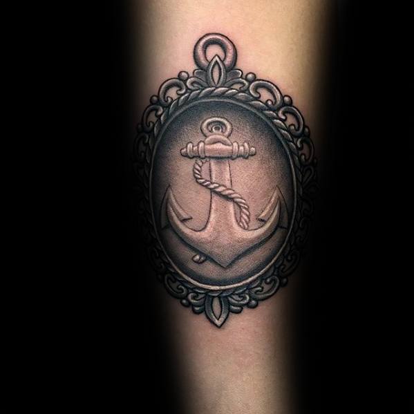 Tattoo of an anchor encased in an ornate oval frame on a person's forearm