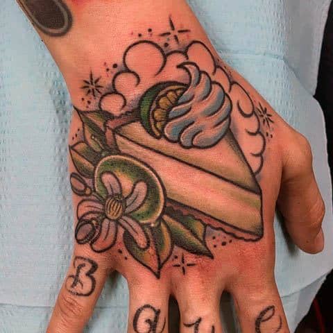 Key lime pie tattoo on the hand with whipped cream, a lime slice, and floral accents, blending traditional tattoo style with a tropical twist