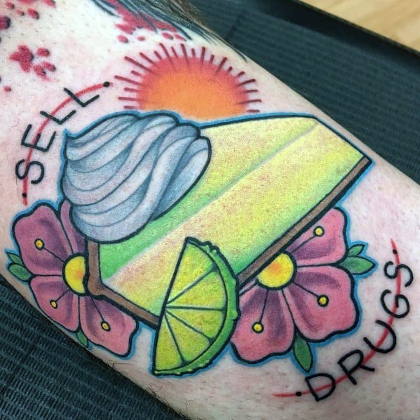 Vibrant key lime pie tattoo with whipped cream, a lime slice, flowers, and a bold sun, featuring the phrase “Sell Drugs” in a playful style
