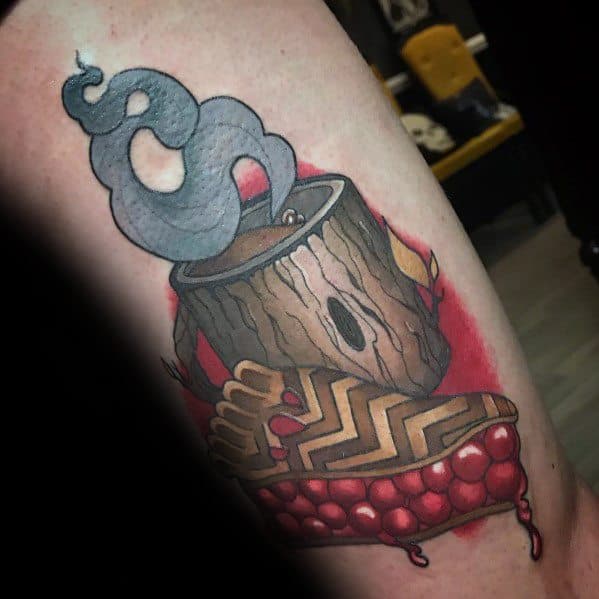 Twin Peaks-inspired tattoo featuring a steaming coffee cup in a log and a dripping cherry pie slice with a zigzag pattern, blending mystery and nostalgia