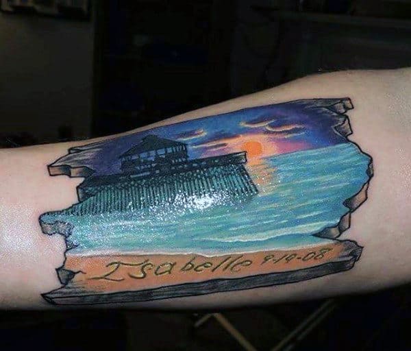 Pier And Sunset On Driftwood Tattoo On Mans Forearm
