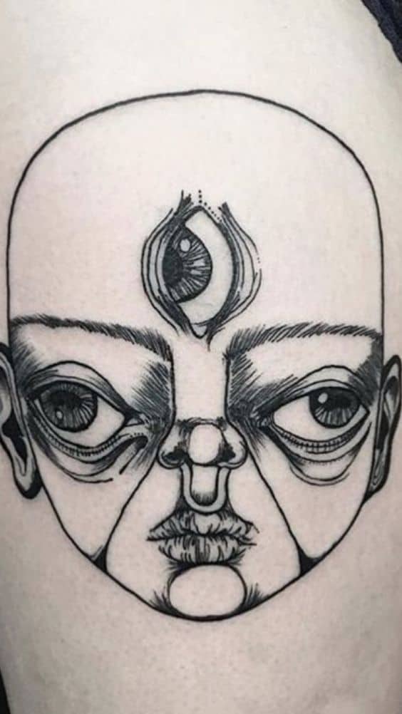 Black ink tattoo of a surreal baby-like face with exaggerated features and a third eye on the forehead, inked with fine linework.