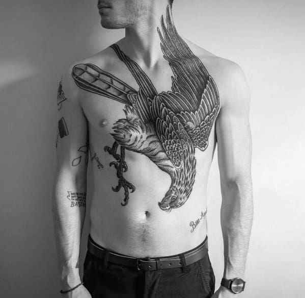 Large blackwork pigeon tattoo across chest and shoulder, in mid-dive with a skeleton key in its beak, symbolizing freedom and hidden truths.
