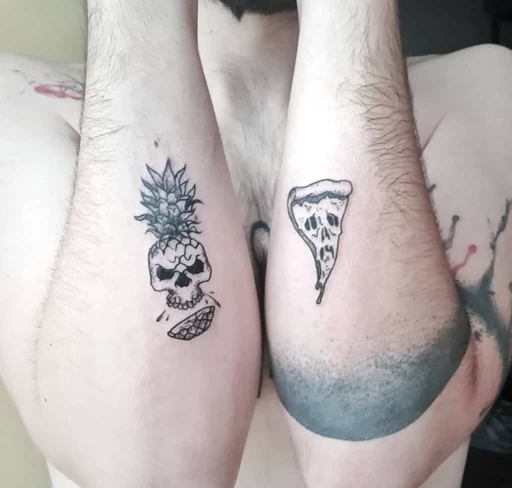Two black ink tattoos on forearms: one of a skull with a pineapple top and a grinning mouth, the other of a melting pizza slice.