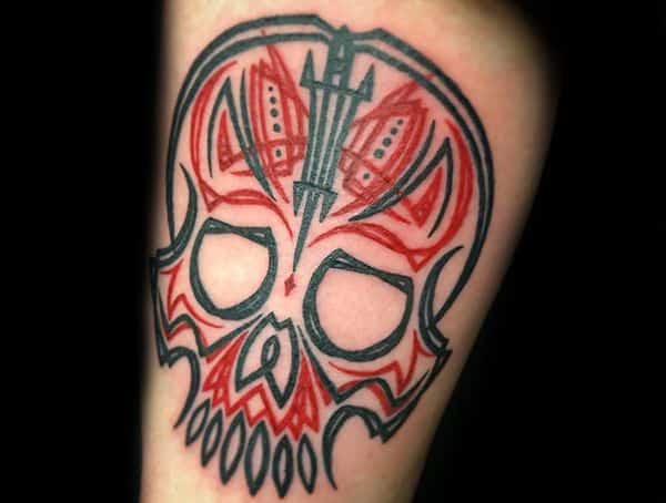 Neo-traditional skull tattoo with bold black outlines and red tribal-style accents, featuring a dagger embedded in the design for a striking effect.