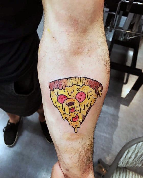 Adventure Time tattoo of Jake the Dog as a slice of pizza with pepperoni, inked on the inner forearm.
