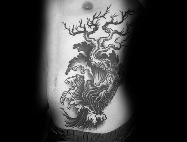 Side torso tattoo for men featuring a dramatic black ink design of crashing waves merging into a twisted, leafless tree.