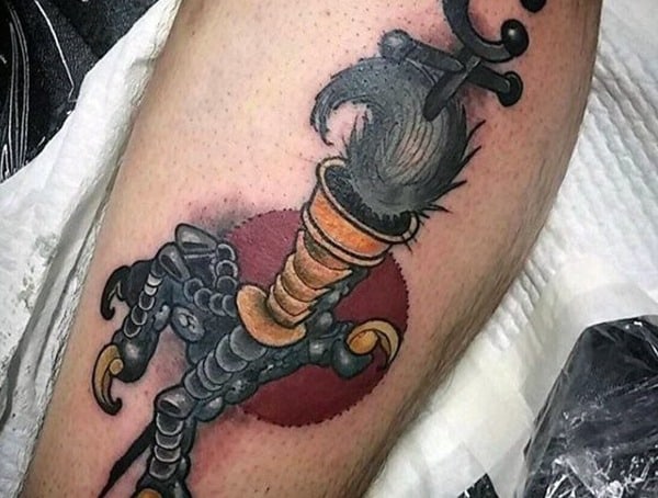 Leg tattoo for men featuring a bold traditional-style design of a bird claw gripping a dagger with a red sun backdrop.