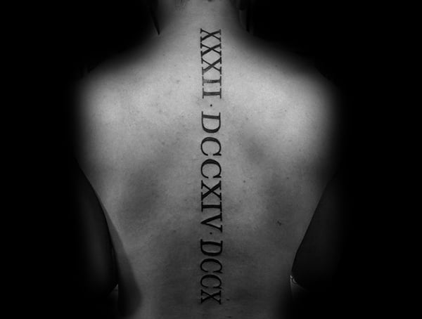 Spine tattoo for men featuring vertical Roman numerals in bold black ink running down the center of the back.
