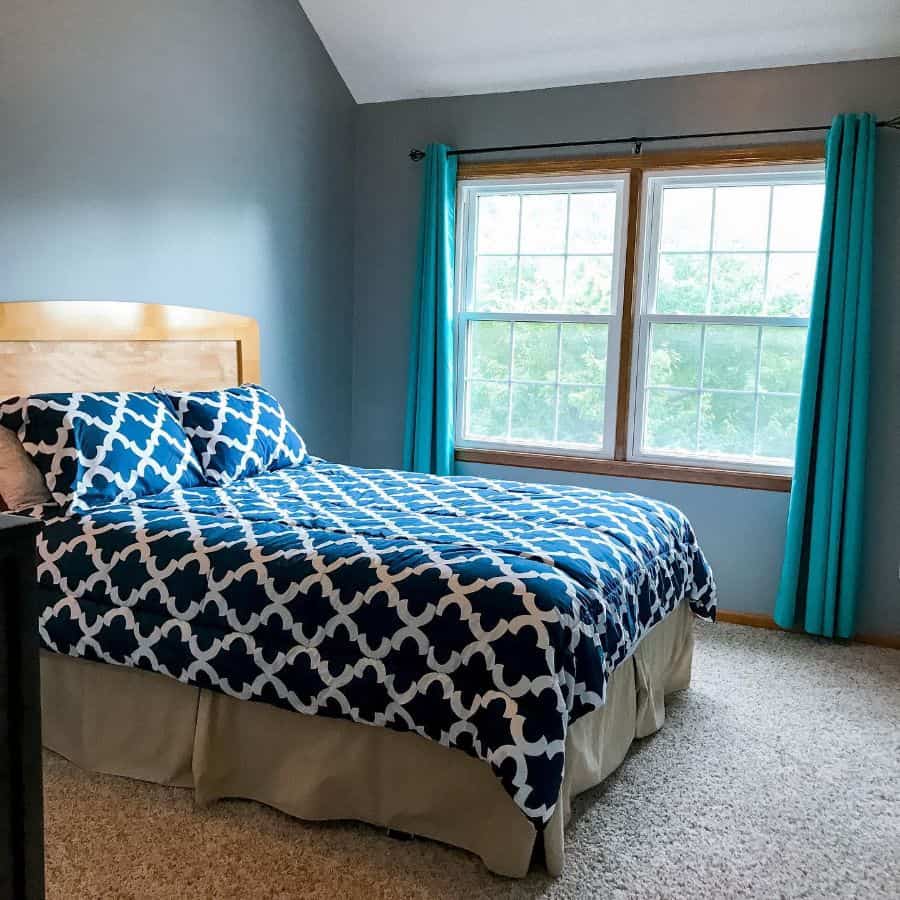 Simple bedroom with blue patterned bedding, teal curtains, and large window.