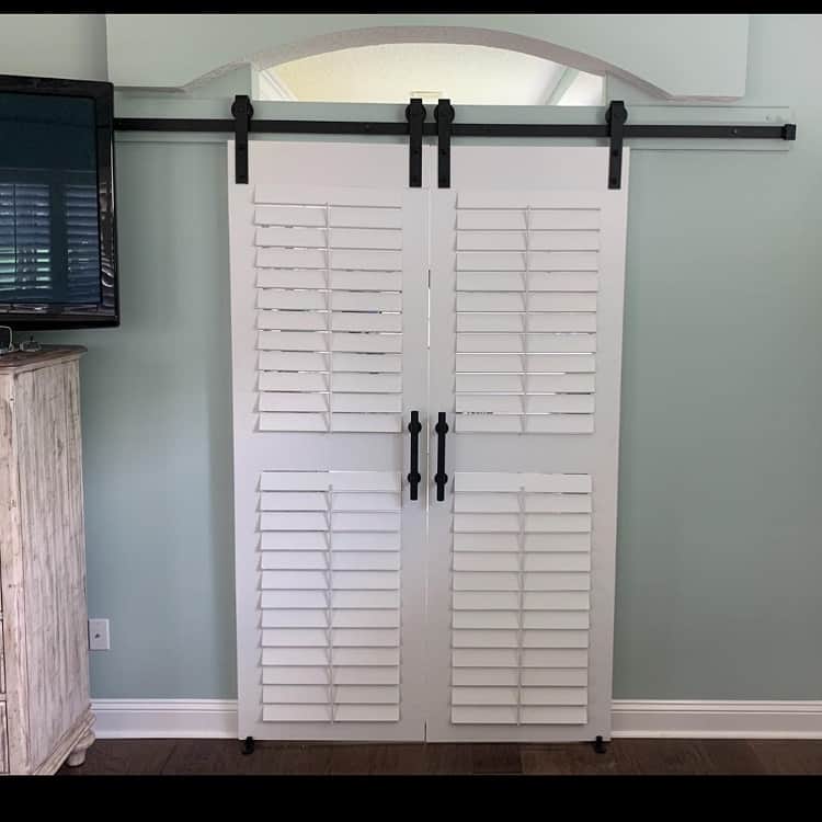White plantation-style sliding French barn doors with shutters and black hardware.