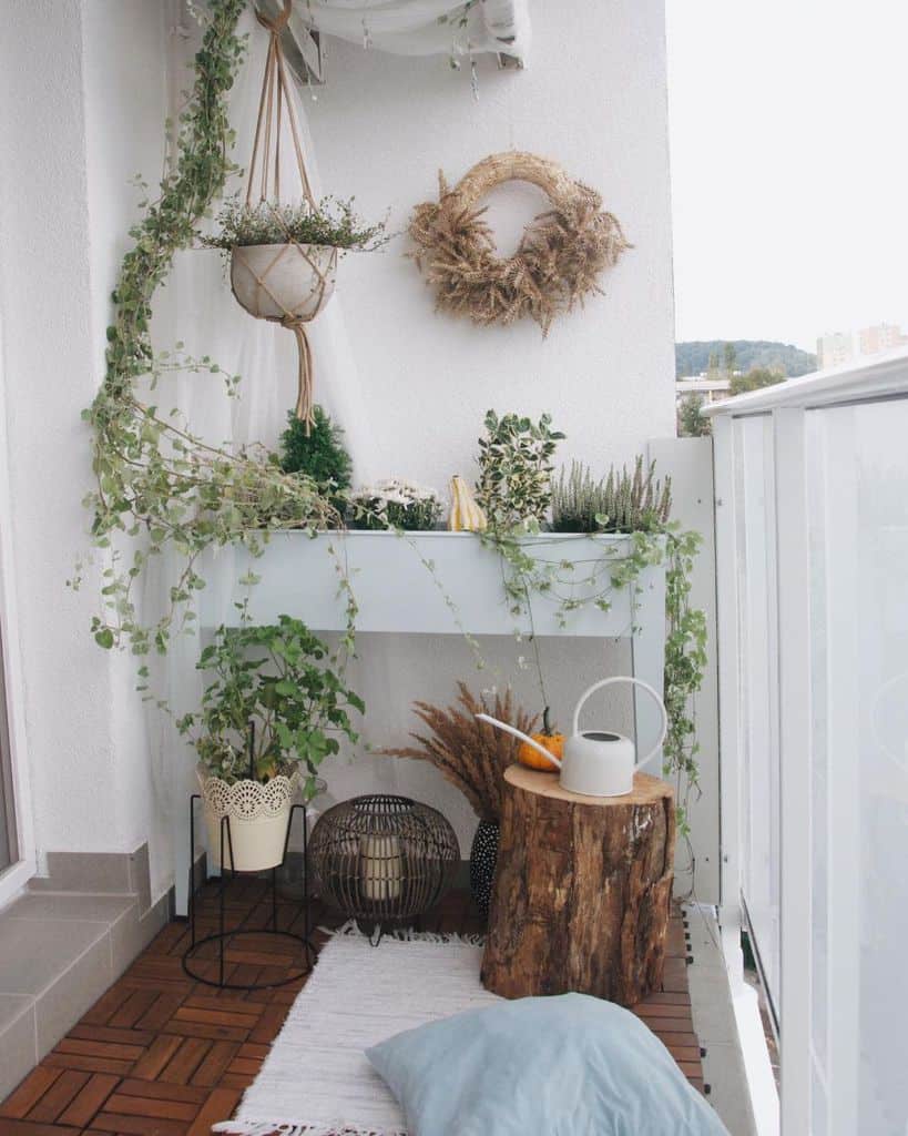 White balcony with hanging plants, potted greenery, a wooden stump table, and cozy decor.