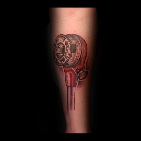 Realistic tattoo of a red pipe threading tool with detailed shading and depth, placed vertically along the forearm.