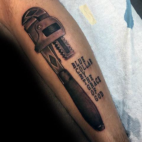 Realistic tattoo of a vintage pipe wrench with the phrase BLUE COLLAR BY THE GRACE OF GOD in bold black lettering beside it.
