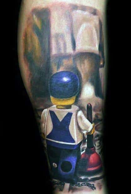 Realistic tattoo of a LEGO-style plumber figure holding a plunger, facing a toilet in a playful and imaginative scene.