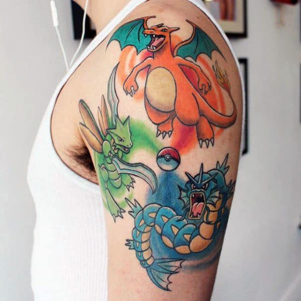 Upper arm tattoo featuring Charizard, Scyther, and Gyarados in vibrant colors with a Poké Ball centered between them in battle stance.