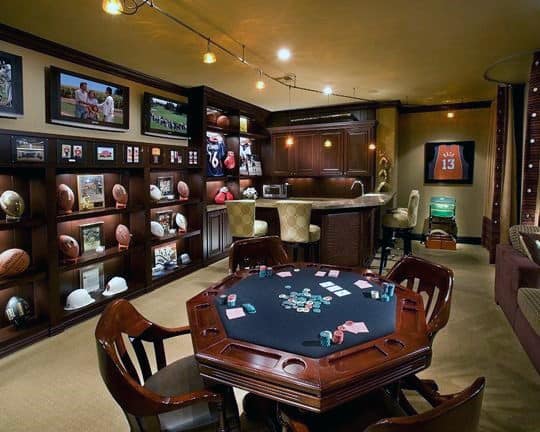 Luxury man cave with poker table, sports memorabilia, and bar area with high stools
