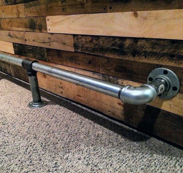 Polished silver steel pipe foot rail attached to a rustic wooden bar with carpeted flooring.