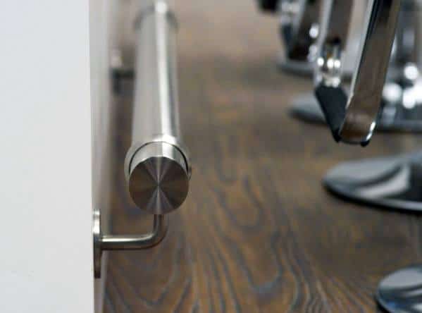 Polished stainless steel foot rail with sleek, modern design attached to a bar on dark wood flooring.