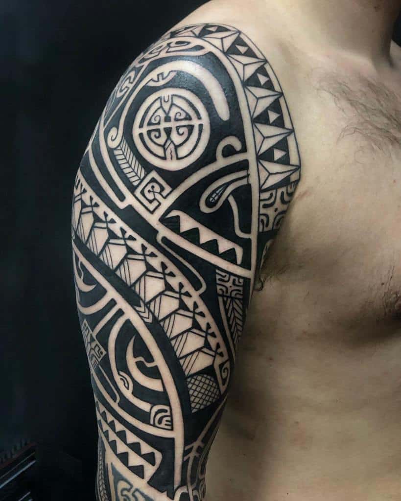 A person with a detailed tribal sleeve tattoo covering the shoulder and upper arm, featuring geometric patterns and symbols