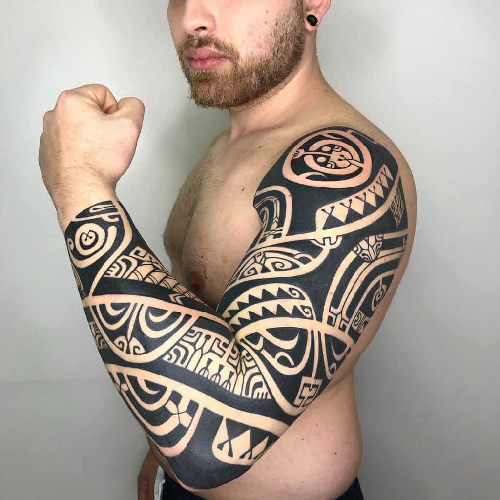 Bold Polynesian-inspired full sleeve and shoulder tattoo featuring intricate black patterns and negative space designs