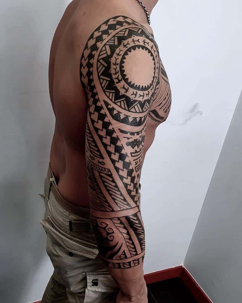 Full-sleeve Polynesian tattoo featuring bold black geometric patterns, circular designs, and intricate tribal details from shoulder to wrist